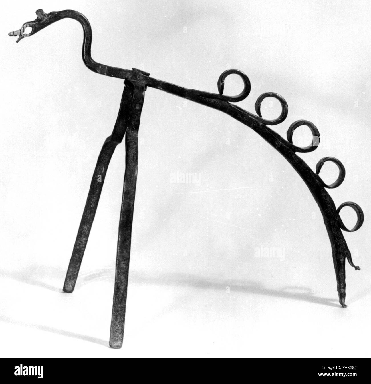 Spit Bracket. Culture: Spanish (?). Dimensions: Overall: 15 3/4 x 10 x 18 in. (40 x 25.4 x 45.7 cm). Date: 16th century.  Although Spanish, particularly Catalan, iron working had reached a level of great artistry by the late Middle Ages, many ordinary household objects continued to be wrought in the traditional and less refined fashion, as is the case with this support for a spit (once part of a pair). It is amusing, however, and its maker demonstrated great inventiveness in transforming the scaly fins of its arched back into rings through which the spit could be inserted at gradual intervals. Stock Photo