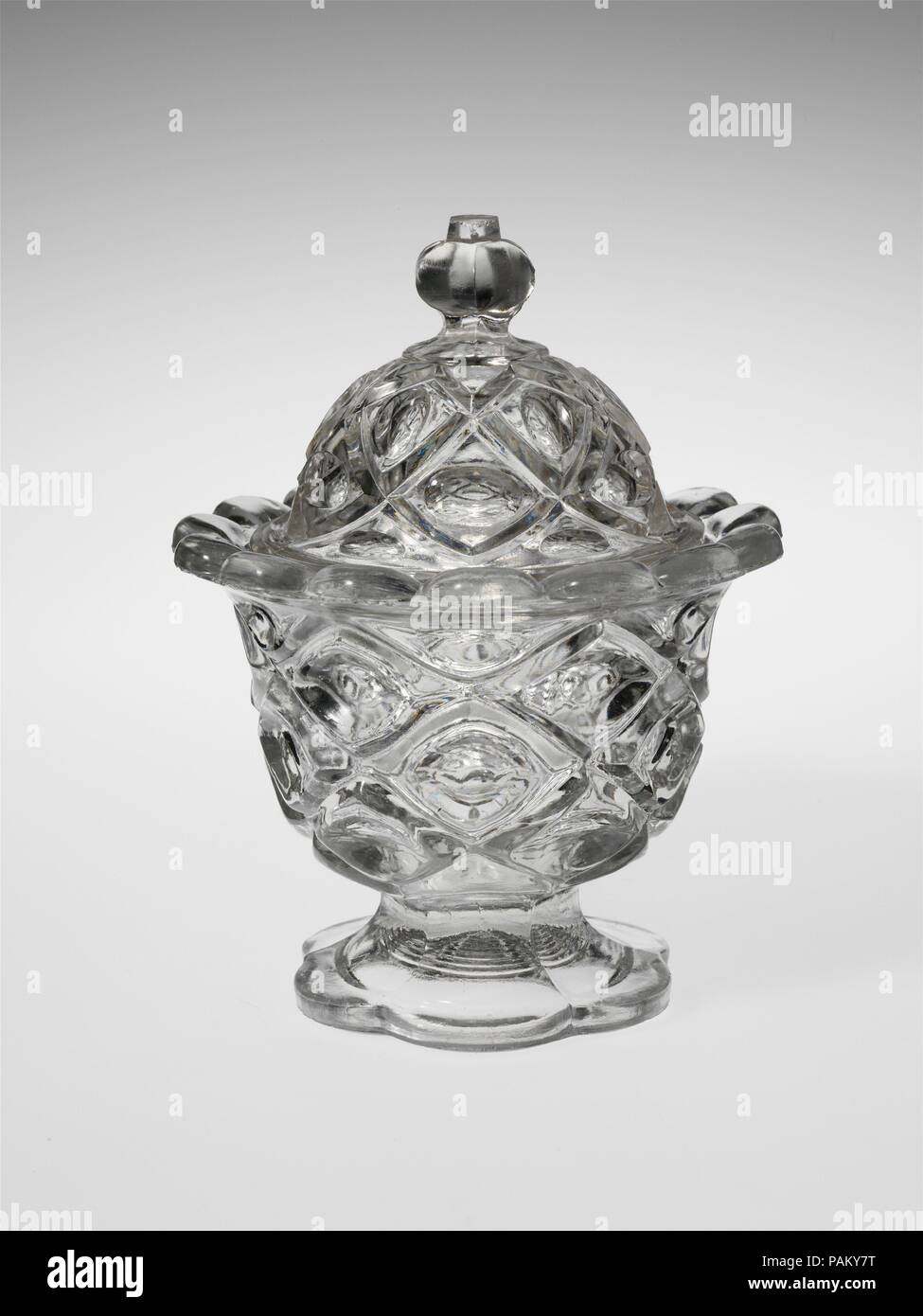 Sugar Bowl. Culture: American. Dimensions: H. 7 in. (17.8 cm); Diam. 5 3/8 in. (13.7 cm). Date: 1850-70.  With the development of new formulas and techniques, glass-pressing technology had improved markedly by the late 1840s. By this time, pressed tablewares were being produced in large matching sets and innumerable forms. During the mid-1850s, colorless glass and simple geometric patterns dominated. Catering to the demand for moderately-priced dining wares, the glass industry in the United States expanded widely, and numerous factories supplied less expensive pressed glassware to the growing  Stock Photo