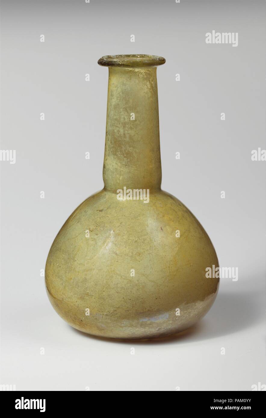 Glass perfume bottle. Culture: Roman. Dimensions: Overall: 5 9/16 in. (14.1 cm)  Diam.: 3 5/8 x 1 3/8 in. (9.2 x 3.5 cm). Date: 1st-2nd century A.D..  Translucent yellow green.  Uneven rim folded out, over, and in; flaring mouth; cylindrical neck, expanding slightly downwards, with tooled indent around base; bulbous body; flat bottom.  Intact; pinprick and larger bubbles, with a few glassy inclusions; limy encrustation and iridescent weathering on interior. Museum: Metropolitan Museum of Art, New York, USA. Stock Photo