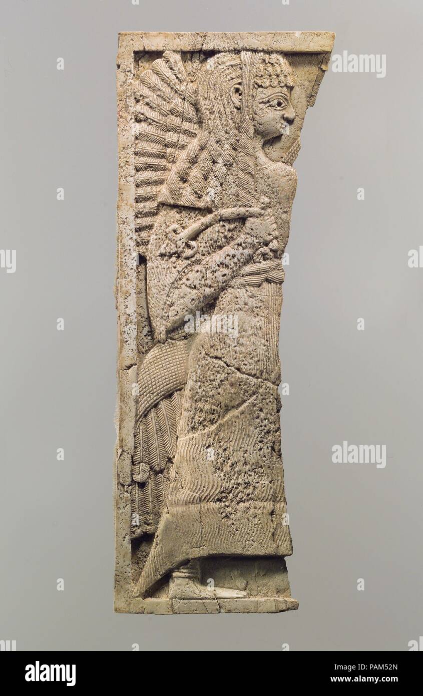 Furniture plaque carved in relief with standing woman. Culture: Assyrian. Dimensions: 9.96 x 3.74 in. (25.3 x 9.5 cm). Date: ca. 9th-8th century B.C..  This ivory panel was found in a storage room in Fort Shalmaneser, a royal building at Nimrud that was used to store booty and tribute collected by the Assyrians while on military campaign. Like many other panels from the same storage room, it was part of a chair or couch back or the headboard of a bed. Twenty pieces of furniture were discovered stacked in orderly rows in this room, where they had been stored before the destruction of the Assyri Stock Photo