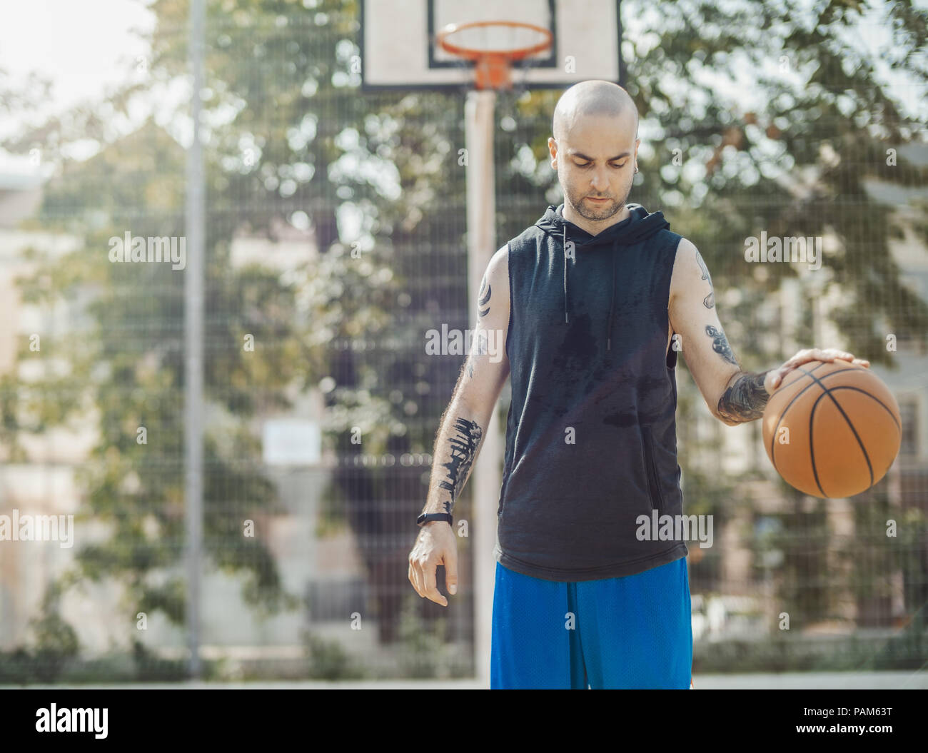 Bald attractive man playing basketball on the basketball court. Man is on focus and foreground, background is blurred. Stock Photo