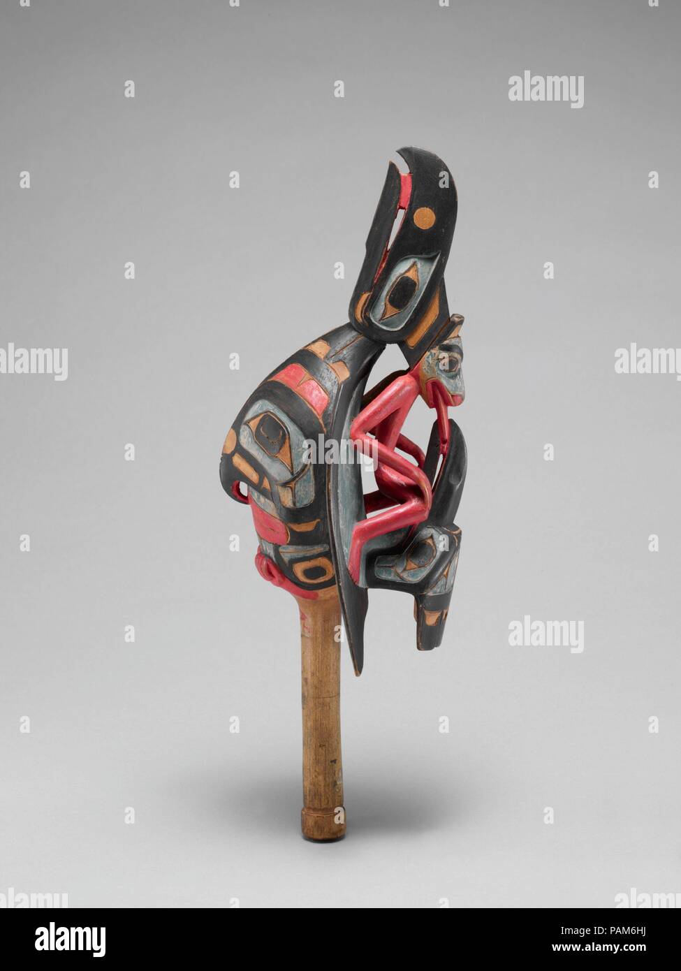 Raven rattle. Culture: Native American (Tsimshian). Dimensions: 12 3/16 × 4 1/16 × 4 1/8 in. (31 × 10.3 × 10.5 cm). Date: 19th century.  Most often associated with shamanic practices on the Northwest Coast, raven rattles are held oriented with the bird's beak pointing down when used in dance. Additionally, rattles like this are used to channel a shaman's spirit guide and can be used in healing ceremonies. Much of the symbolism associated with this rattle comments on the transmission of power from one figure to the next--the raven to humankind in general (as oral tradition states) and the kingf Stock Photo