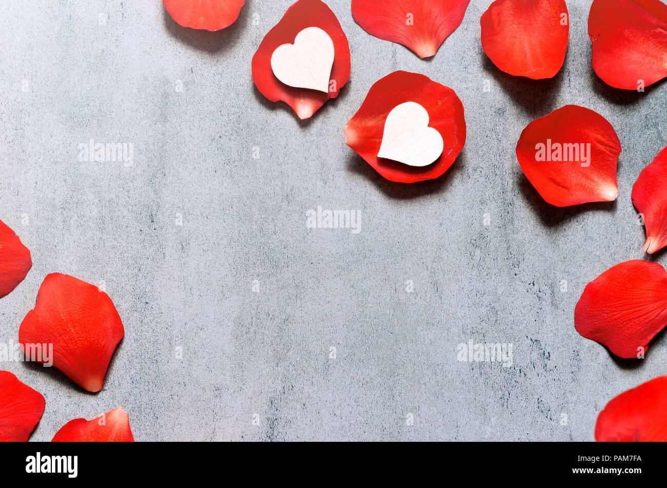 White heart decoration on red rose petals background on grey table. Romance concept. Flat lay, top view. Stock Photo