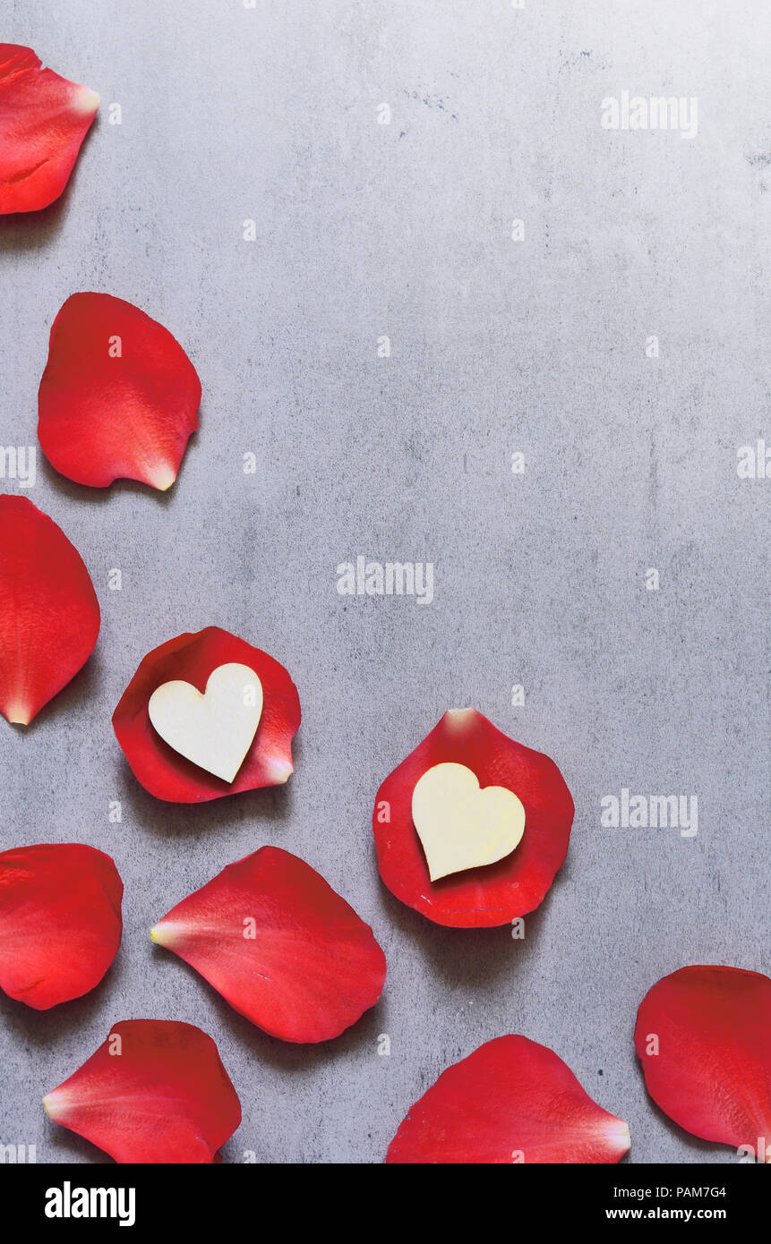 White heart decoration on red rose petals background on grey table. Romance concept. Flat lay, top view. Stock Photo