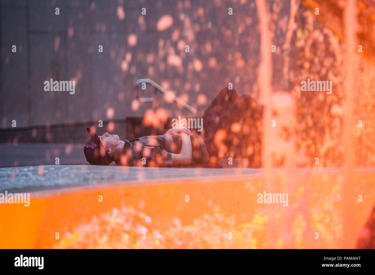 A young male lies down by a colourfiully lit fountain in downtown Montreal, Quebec. Stock Photo