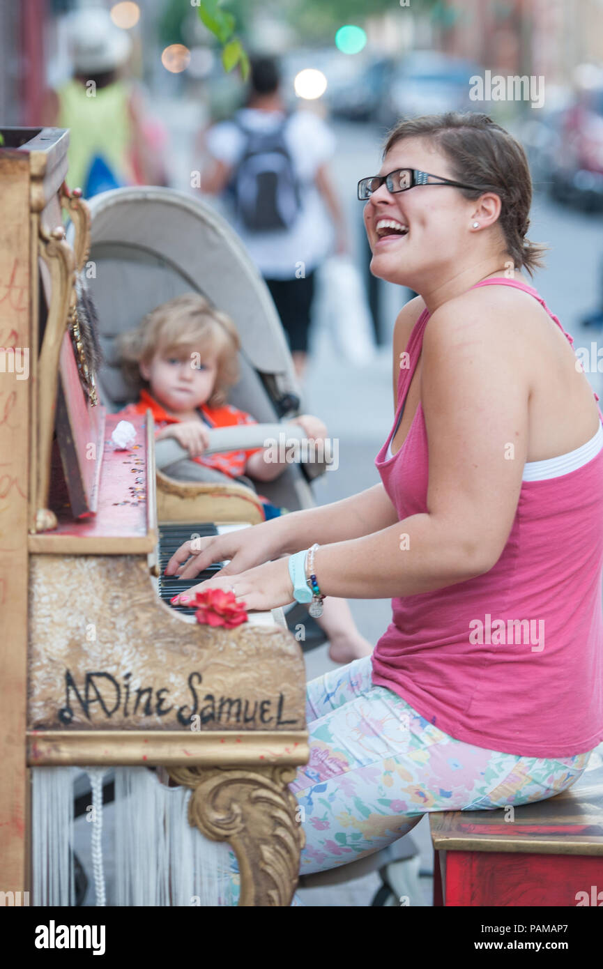 A street performer plays the piano in the street as her child looks on in downtown Montreal, Quebec. Stock Photo