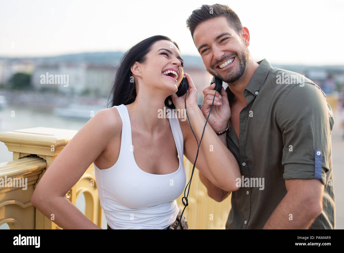 Happy young couple sharing headphones and laughing in city outdoors Stock Photo