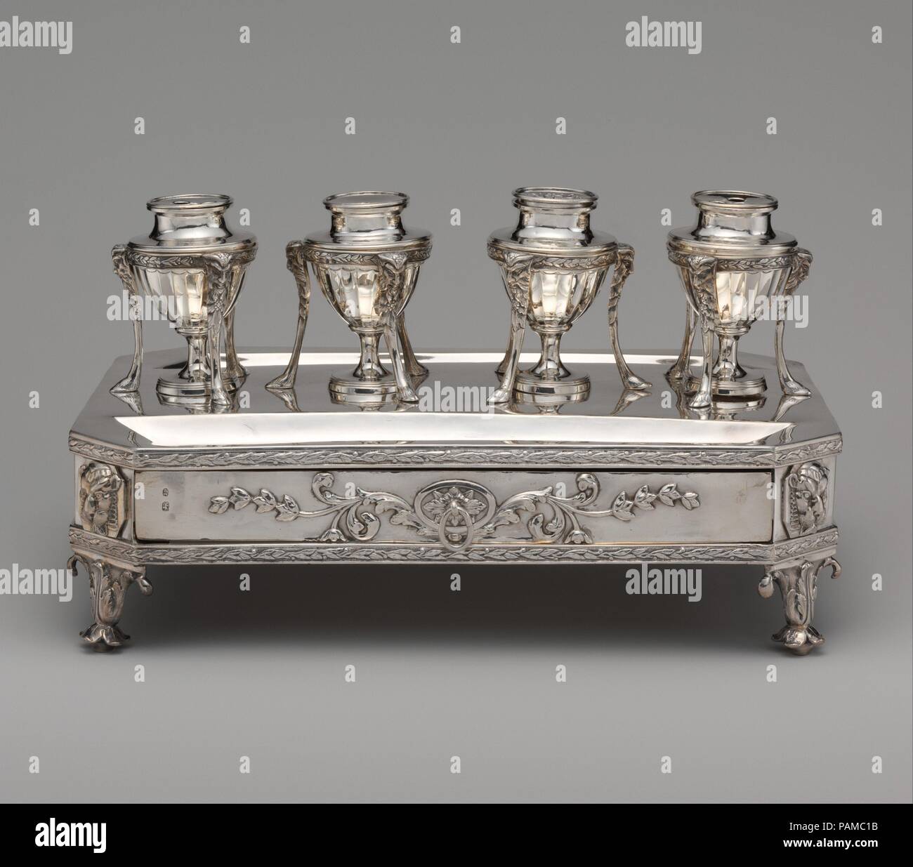 Inkstand. Culture: British, London. Dimensions: Width: 13 3/16 in. (33.5 cm). Maker: John Plimmer (active 1771-1803). Date: 1802.  The inkstand has four vase-shaped containers supported in tripod frames that suggest, in miniature, the stands of antiquity that Europeans called 'Atheniennes.' Two of the containers have holes in the covers for pens and inks and a third has a pierced design on the cover for sand, which served to dry the ink. The fourth container probably held wafers--small readymade paste-disks for sealing letters. There is a deep slot on each of the long sides for pens and a tray Stock Photo