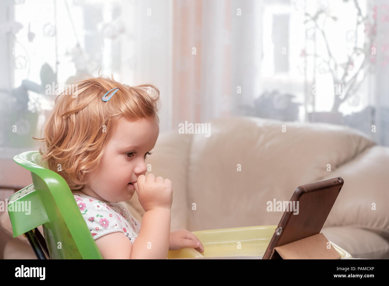 Soft portrait of two years blond kid, girl looking  at a tablet. Family lifestyle. Stock Photo