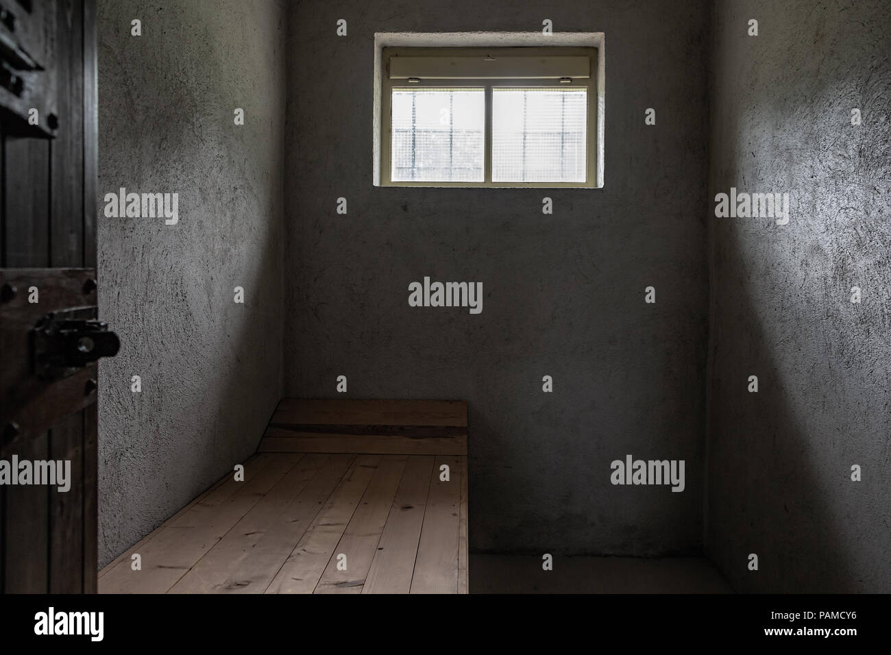 Small prison concrete cell with one small window and one wooden pallet. Stock Photo