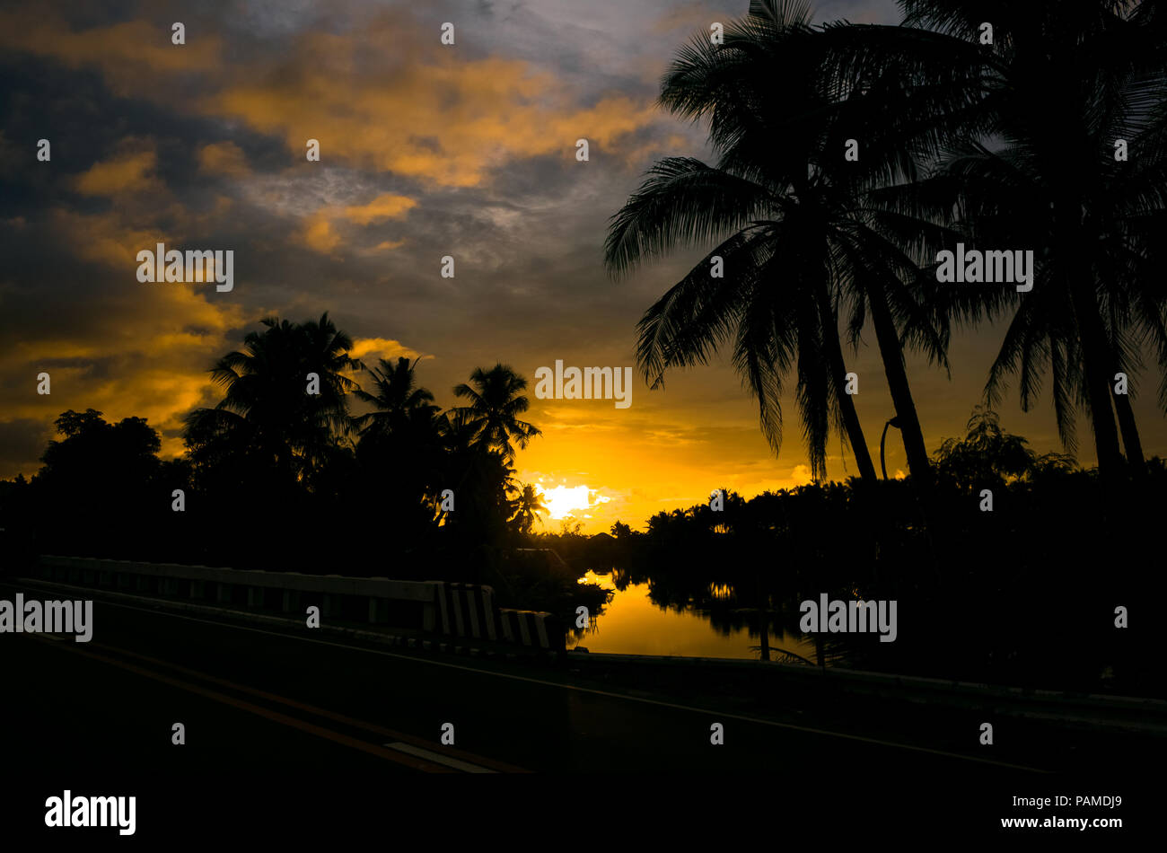Fiery orange island sunrise with coconut tree silhouettes over a tropical lagoon - Taken from the road in Romblon - Philippines Stock Photo