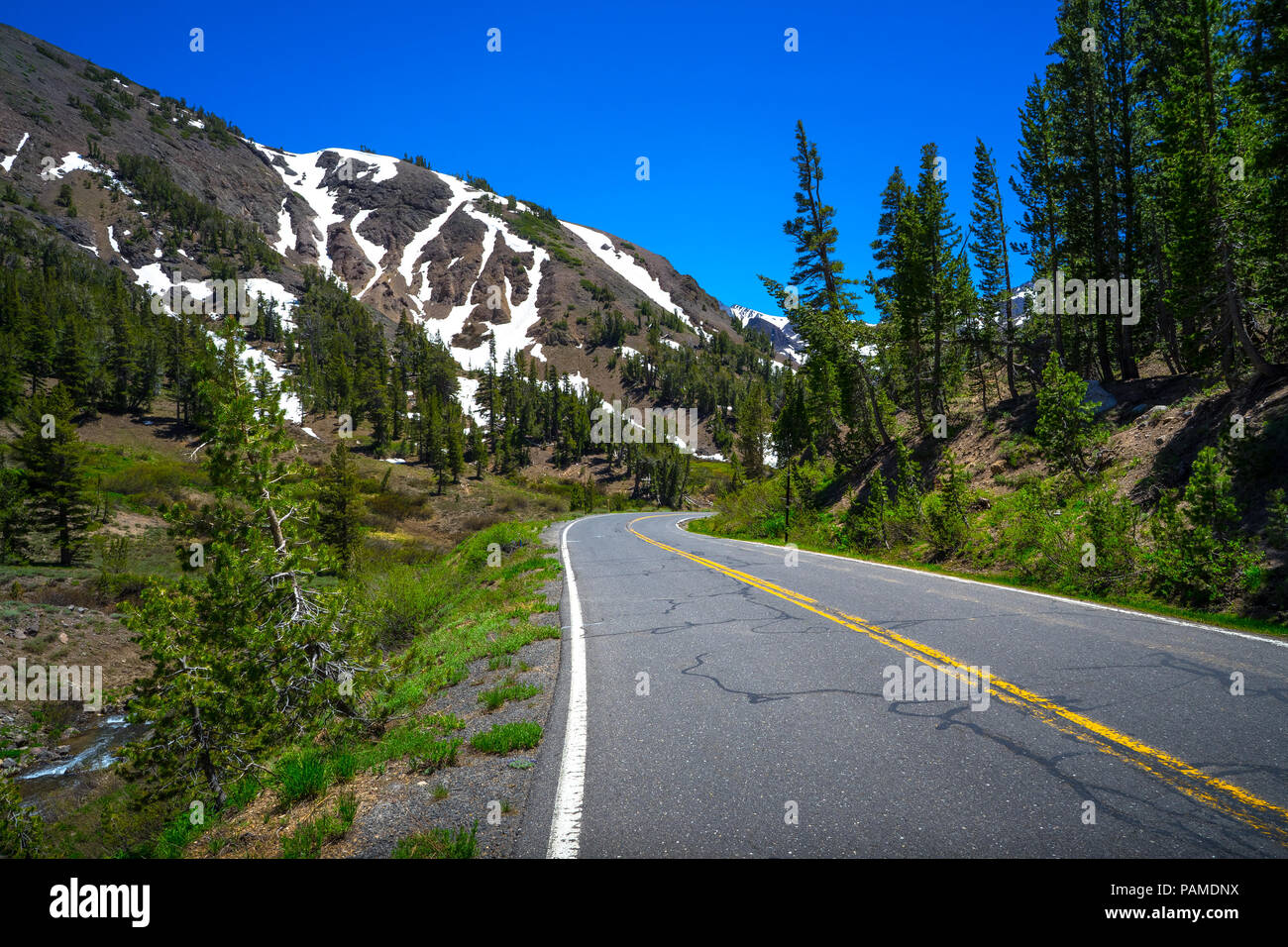 Pavement and double yellow line leading through snowy peaks in Spring - Highway 108 Roadside, California Stock Photo
