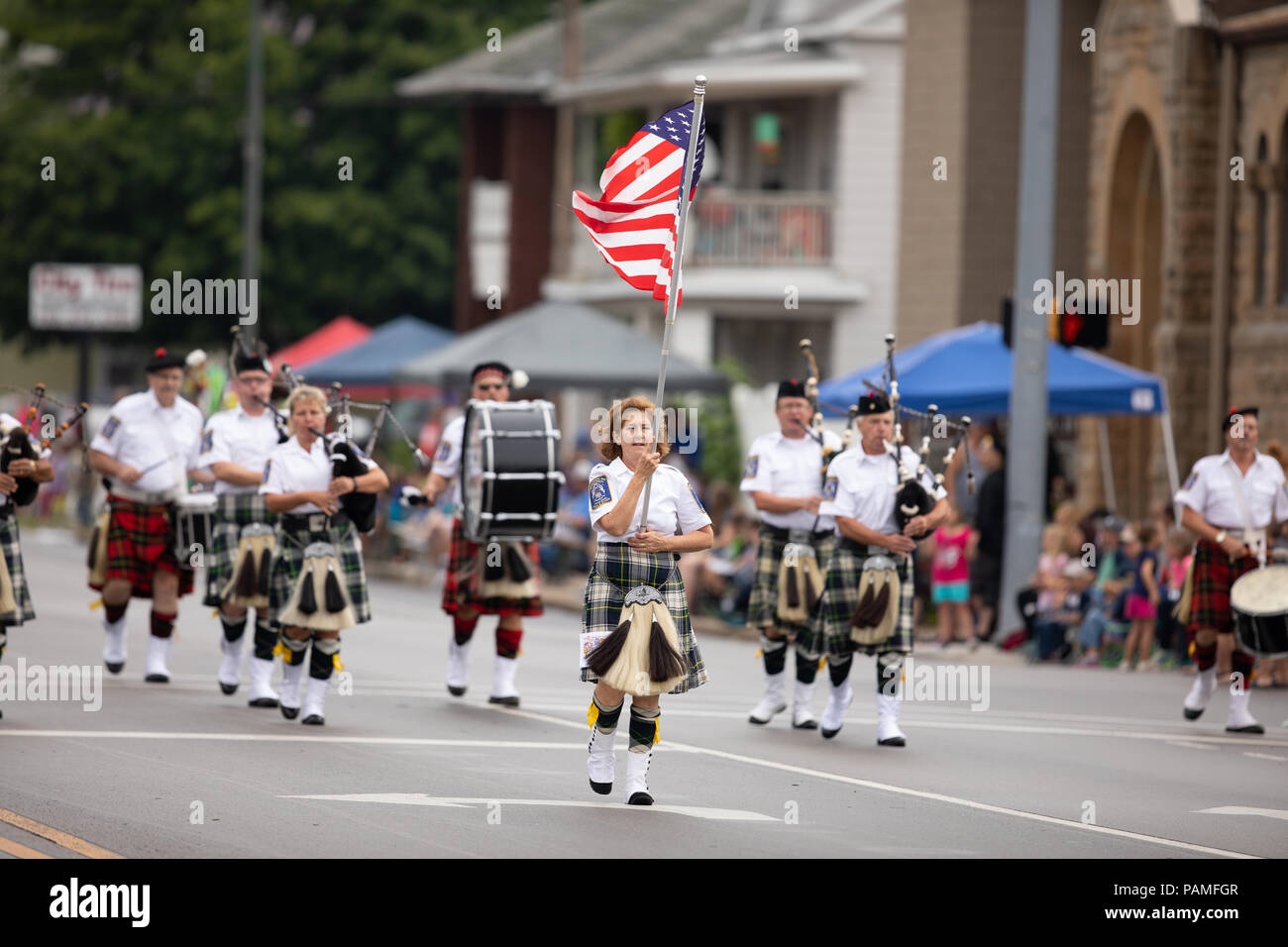 Peru, Indiana, USA - July 21, 2018 Woman carries the American flag leading the Indianapolis 500 Gordon Pipers Horse Shoe Pipes and Drums group of bagp Stock Photo