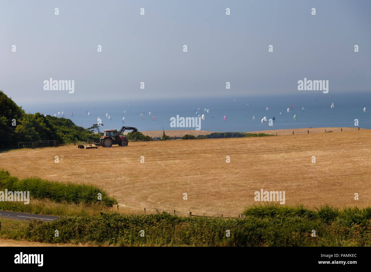 Farm tractor in field with the colourful sails of the Round The Island Race in the background Isle of Wght Hampshire Stock Photo