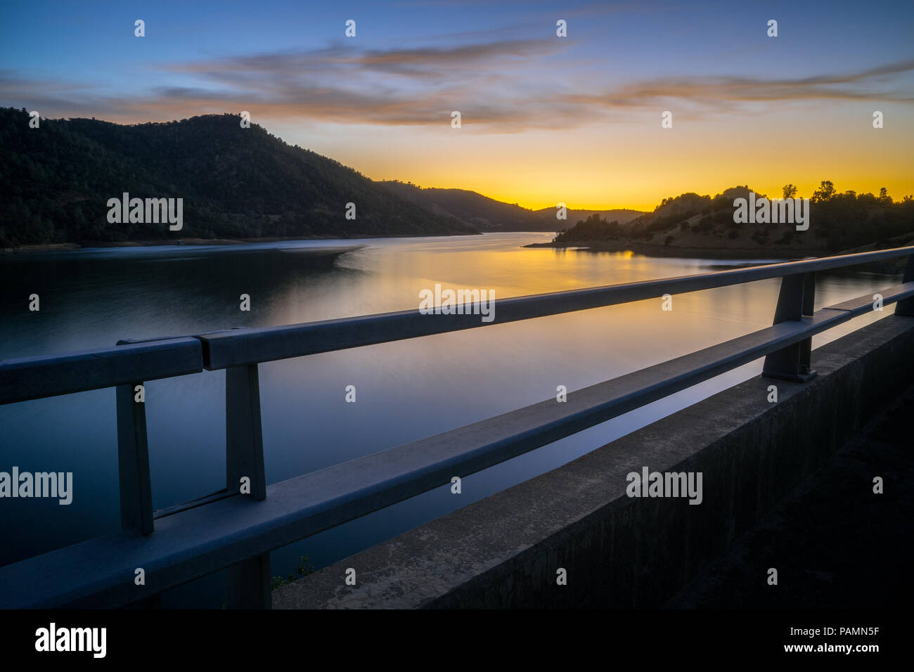 Long exposure shot of Don Pedro Reservoir, with smooth water effect and fiery sunset - Sierra Foothills - Tuolumne County, California Stock Photo