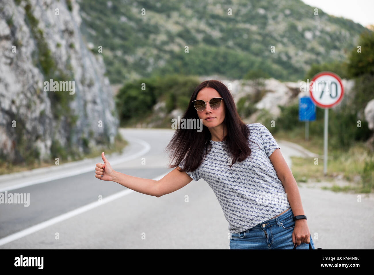 Young backpacking adventurous woman hitchhiking on the road. Traveling backpacks volume, packing essentials. Travel lifestyle. Low budget traveling. Stock Photo