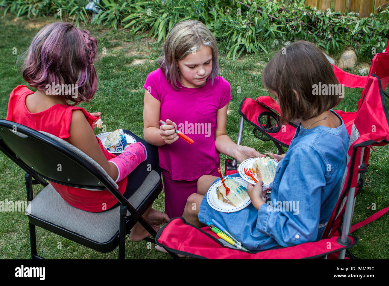 Three young females, two sisters and a cousin, sitting in backyard, on summer day, enjoying birthday cake and talking. Red Top #114, Blue Top #104, Ma Stock Photo