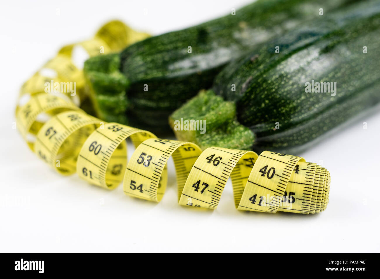 Zucchini on a white table. Tailor measure to measure the waist circumference during the diet