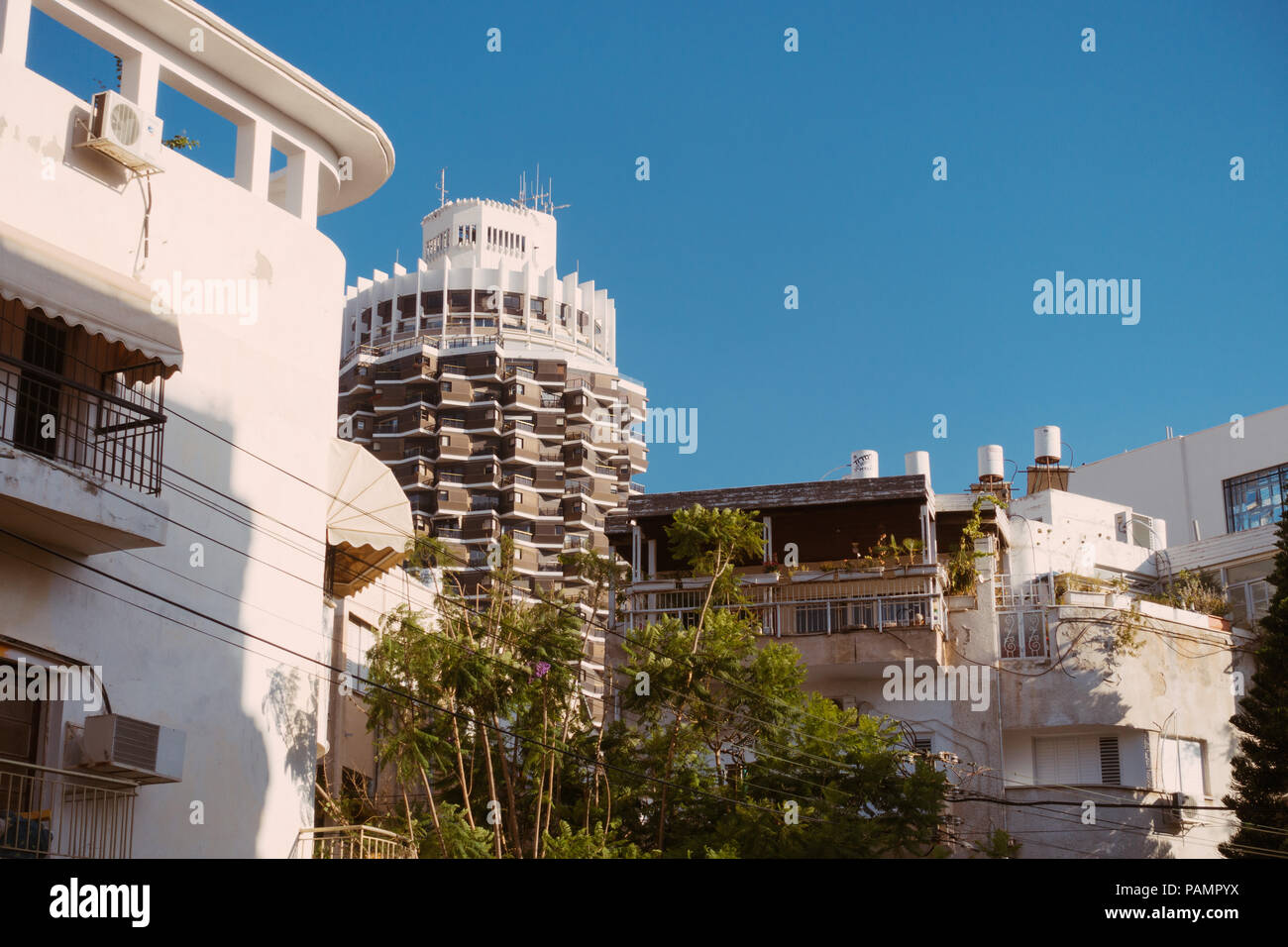 the brown and white cylindrical tower of Dizengoff Center peeks over some white bauhaus-era buildings in Tel Aviv-Yafo, Israel Stock Photo
