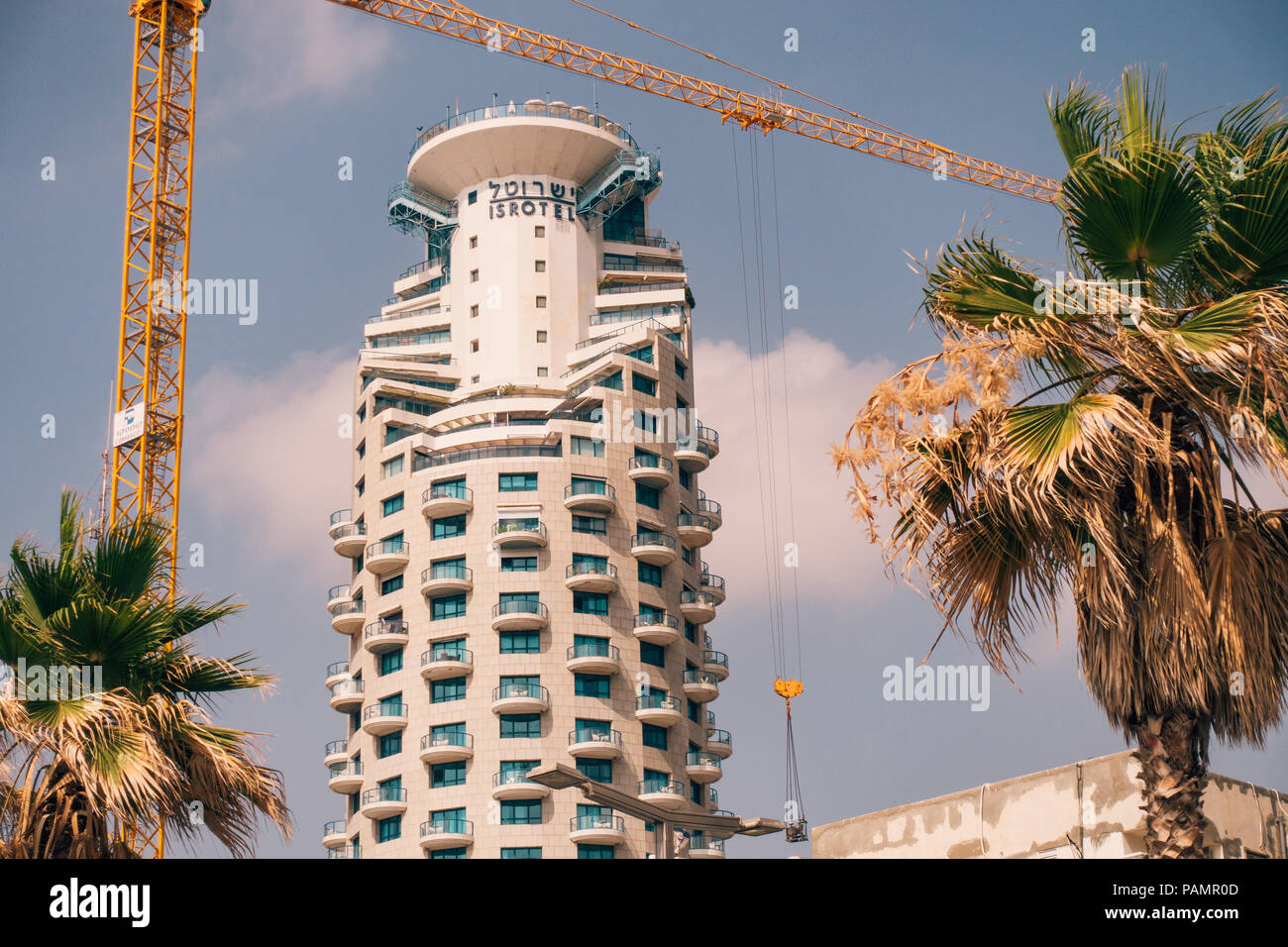 the Isrotel hotel tower building with a crane and palm trees in the foreground in Tel Aviv, Israel Stock Photo
