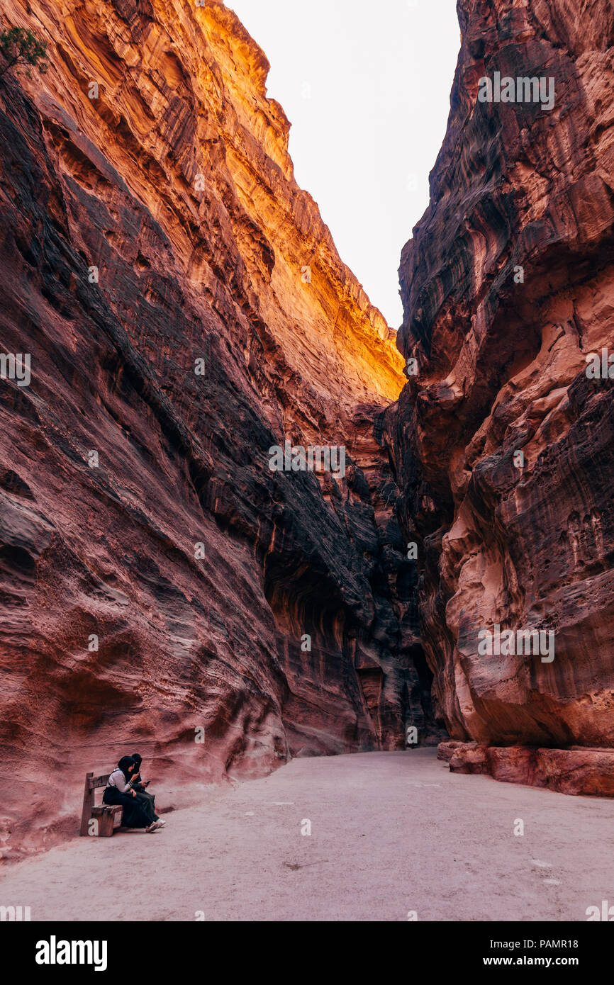 two muslim girls rest and use their phones on the path into Petra, Jordan Stock Photo