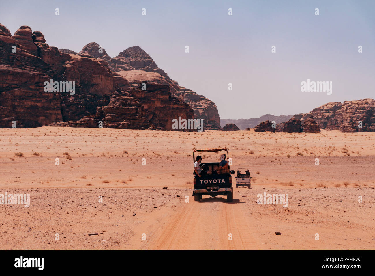 pickup tricks full of tourists drive in a convoy across the red desert sands in the famous Wadi Rum National Park, Jordan Stock Photo
