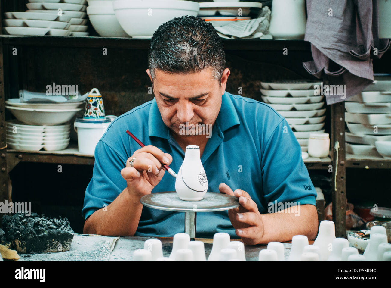 Two Palestinian potters give a coat of decorative paint to some white clay chinaware Stock Photo