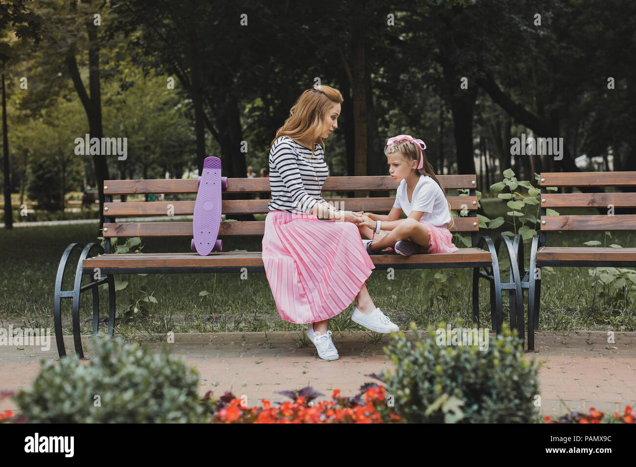 Fashionable mother sitting on bench in the park near her daughter Stock ...