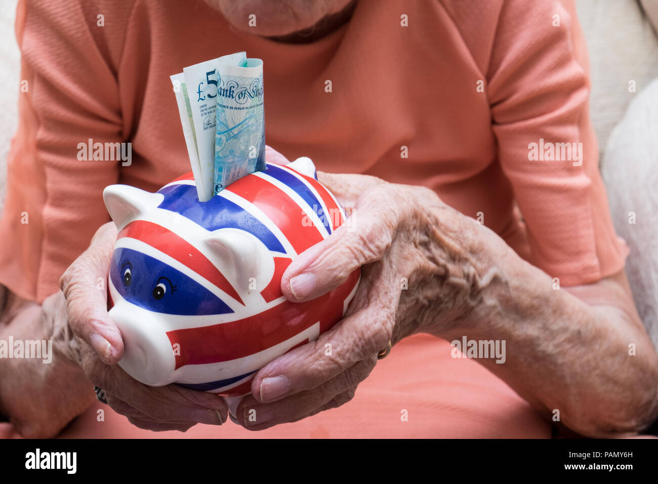 Pension savings, five pound note in piggy bank held by elderly hands Stock Photo