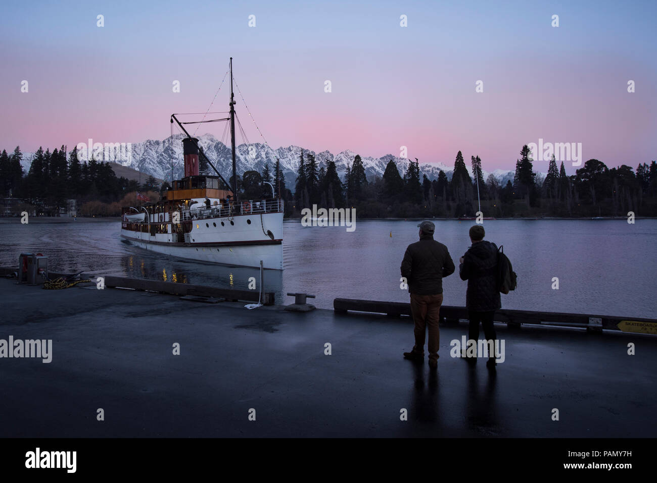 Two people waiting for the steam boat in front of a purple winter sunset, in Lake Wakatipu, Queenstown. Stock Photo