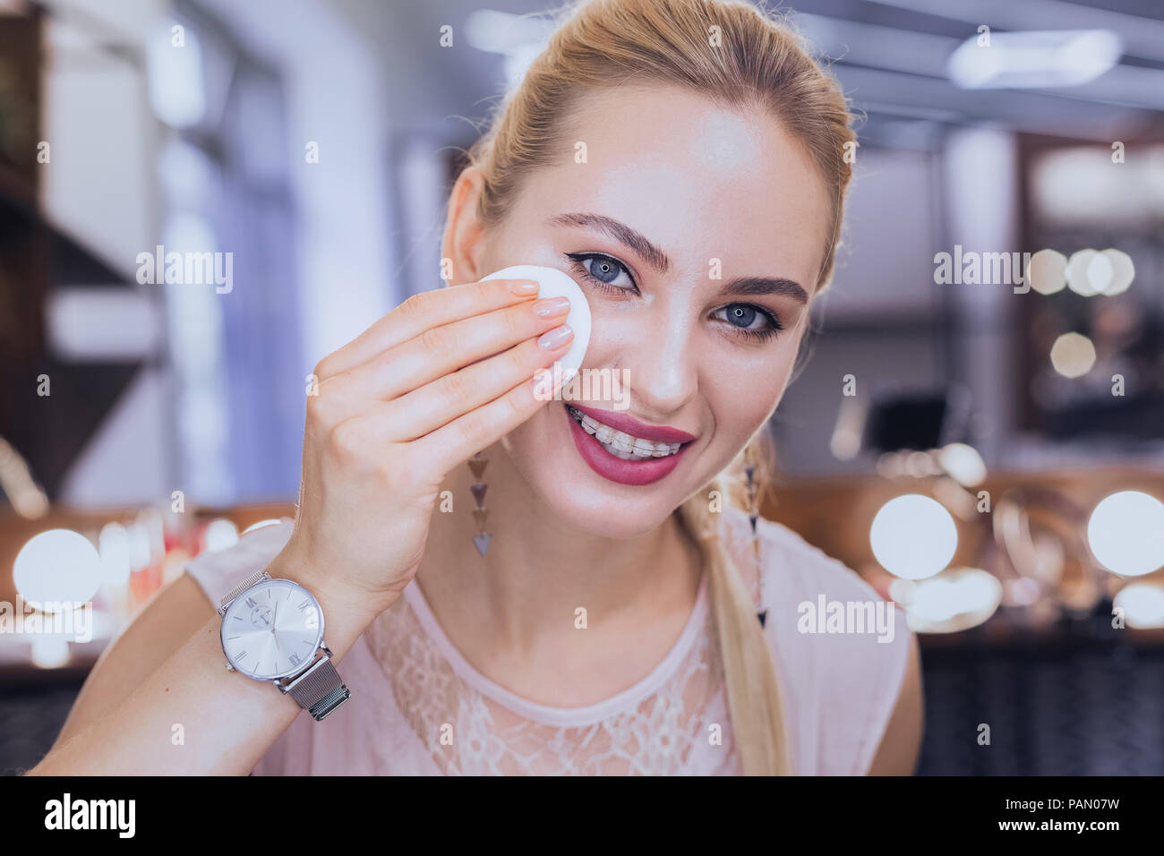 Blonde-haired woman wearing dental brackets taking makeup off Stock Photo