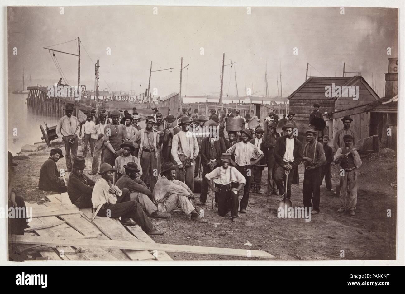 Laborers at Quartermaster's Wharf, Alexandria, Virginia. Artist: Attributed to Andrew Joseph Russell (American, 1830-1902). Dimensions: Image: 13.2 × 20.2 cm (5 3/16 × 7 15/16 in.). Former Attribution: Formerly attributed to Mathew B. Brady (American, born Ireland, 1823?-1896 New York). Date: 1863-65.  The United States Quartermaster's office managed the supply, warehousing, and distribution of food, fuel, ordnance, medical supplies, forage for animals, and even mail delivery for the army. This extraordinary view shows a group of emancipated slaves who worked as paid laborers for the army alon Stock Photo