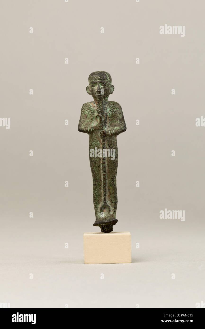 Ptah. Dimensions: H. 8.6 cm (3 3/8 in.); W. 2.5 cm (1 in.); D. 2.1 cm (13/16 in.)  H. (with tang): 8.8 cm (3 7/16 in.). Date: 664-30 B.C..  This statuette depicts Ptah, the chief god of Egypt's capital city Memphis and master craftsman of the gods. He is easy to identify by his tight-fitting cap, straight beard (different from the usual curved divine beard on other gods), and enveloping mummiform garment. The garment has a stiff upper edge along the back of the neck, a feature that occurs with some regularity also on Osiris statuettes, but its meaning is unclear. He is richly adorned with a br Stock Photo