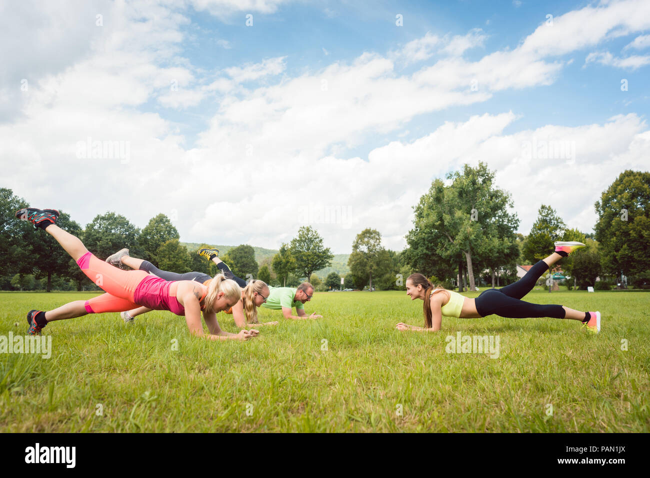 Family planking outdoors in meadow with fitness teacher Stock Photo