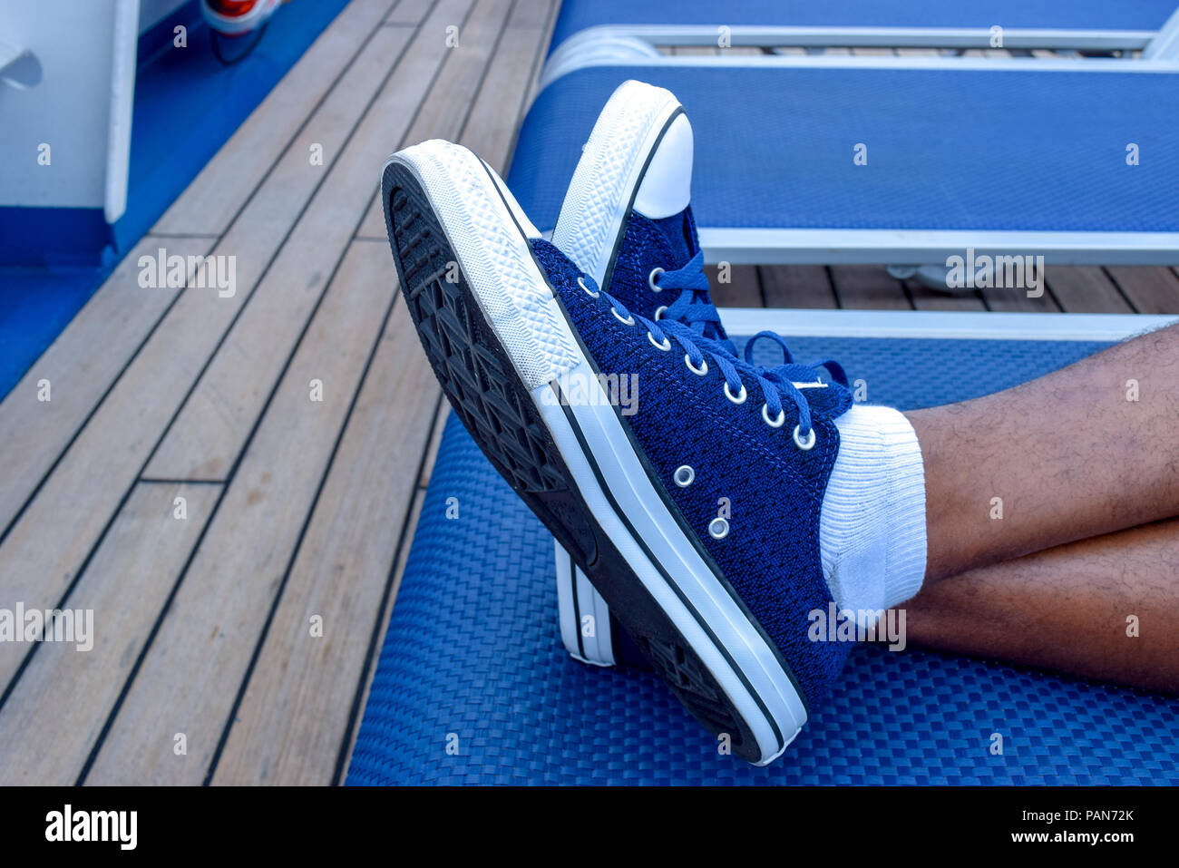 Relaxation. Male feet crossed, wearing blue sneakers, in lounge chair Stock  Photo - Alamy