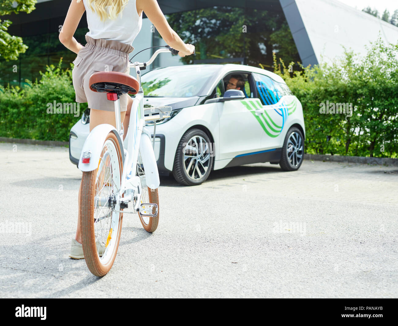 Woman with bicycle in front of electric car Stock Photo