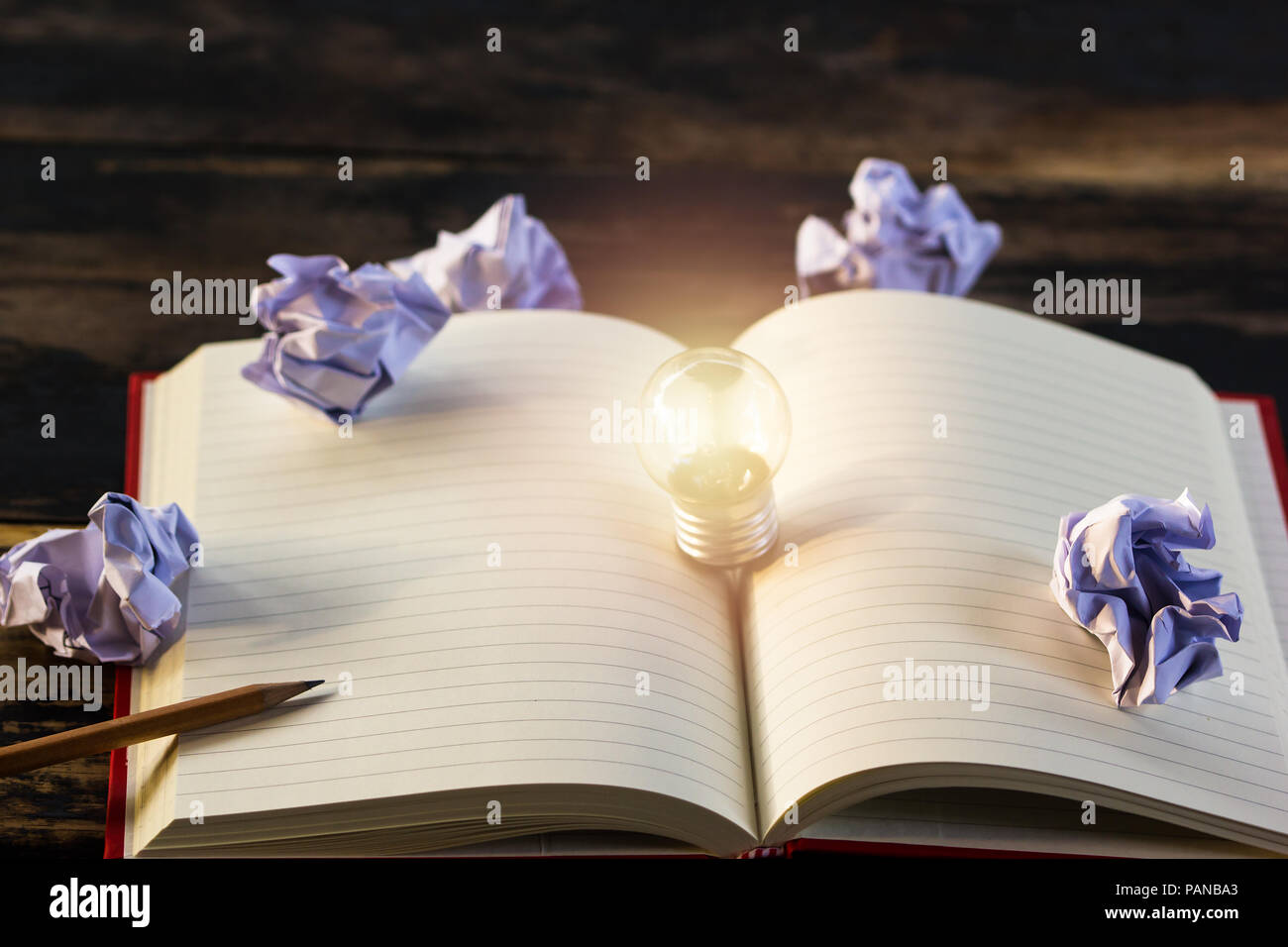 Concept idea. Growing light bulb on vintage book with crumpled papers and pencil. Copy space for your text. conceptual great ideas are always availabl Stock Photo