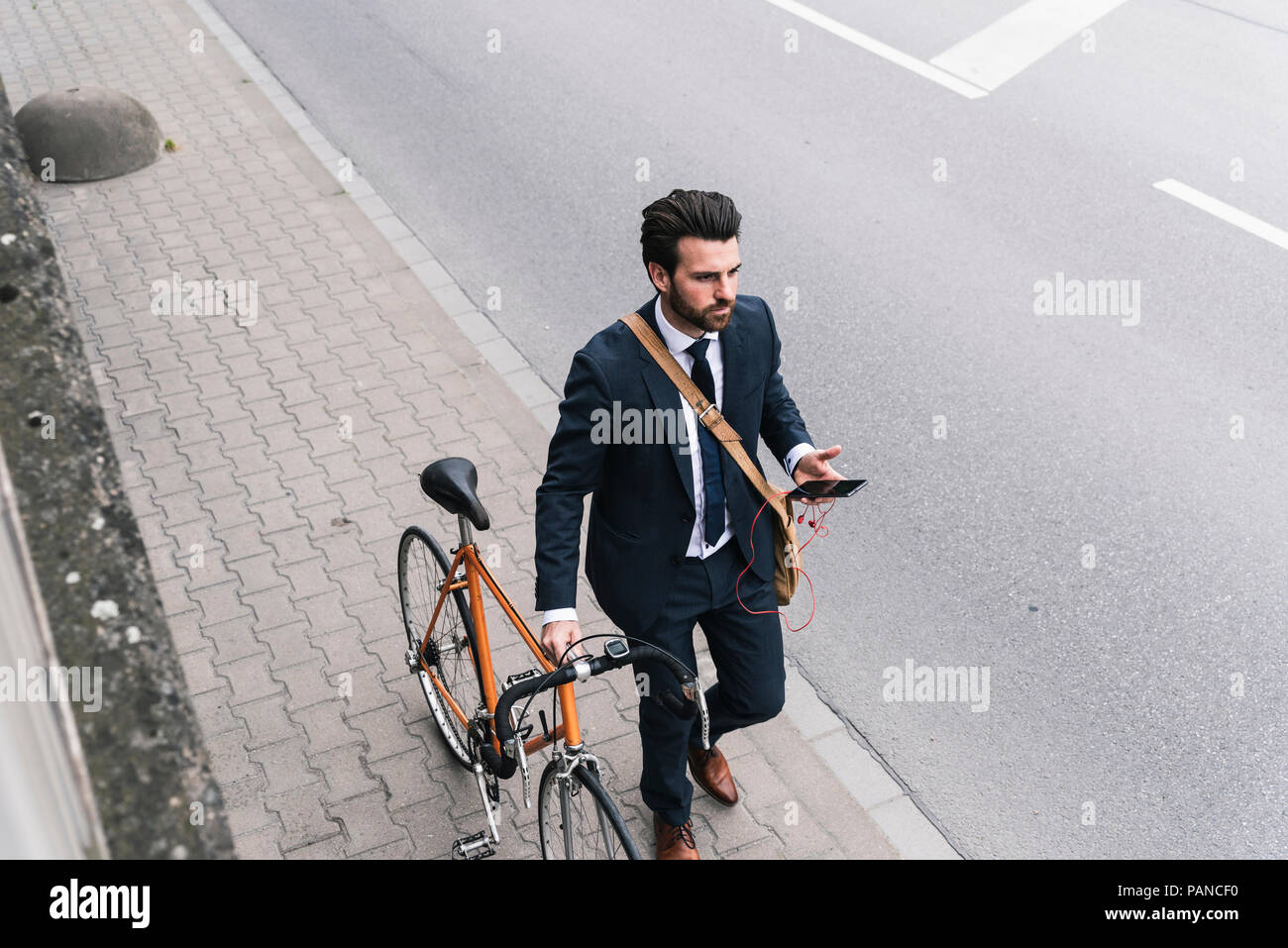 Businessman with bicycle and cell phone walking at the street Stock Photo