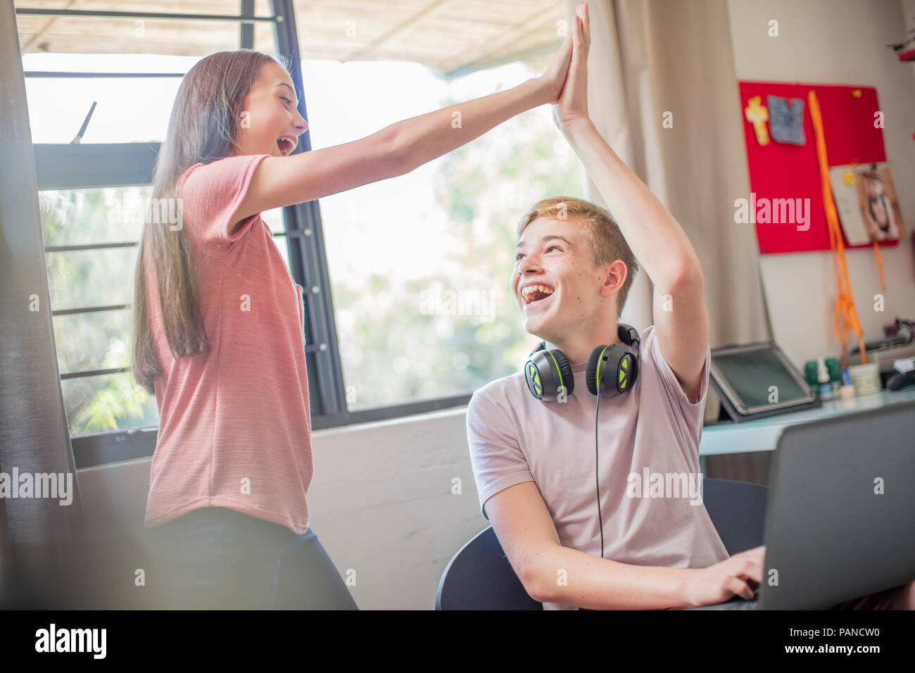 Happy teenage girl and boy with laptop high fiving Stock Photo
