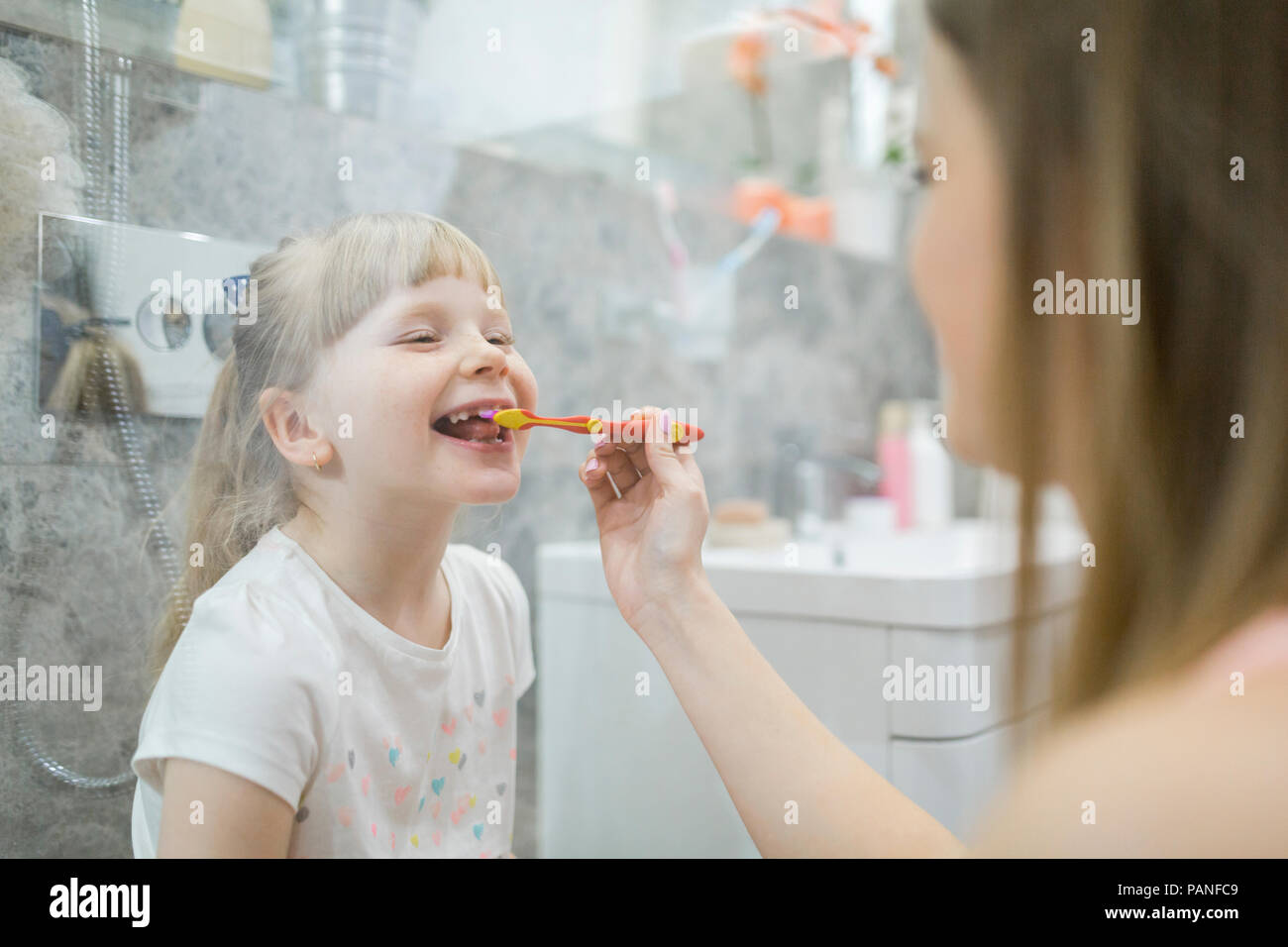 Mother brushing teeth of her daughter in bathroom Stock Photo