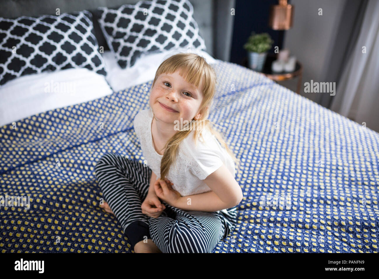 Blond little girl sitting on bed, smiling Stock Photo - Alamy