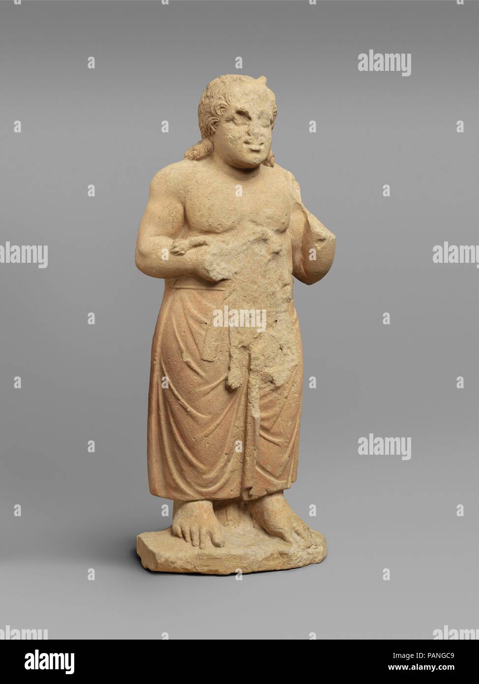 Limestone statue of a god. Culture: Cypriot. Dimensions: Overall: 23 1/2 x 9 1/8 x 5 1/4 in. (59.7 x 23.2 x 13.3 cm). Date: 3rd century B.C..  The identity of this young plump figure with horns at his forehead and a lion in his right hand is uncertain. Although Herakles is usually shown with a lion, statues of the young Herakles are more likely to show him with the snake that he strangled while still in the cradle. Moreover, Herakles does not appear with animal horns. Possibly Bes, an Egyptian god with a lion's face, is shown here in a Cypriot adaptation. On Cyprus, Bes is sometimes shown with Stock Photo