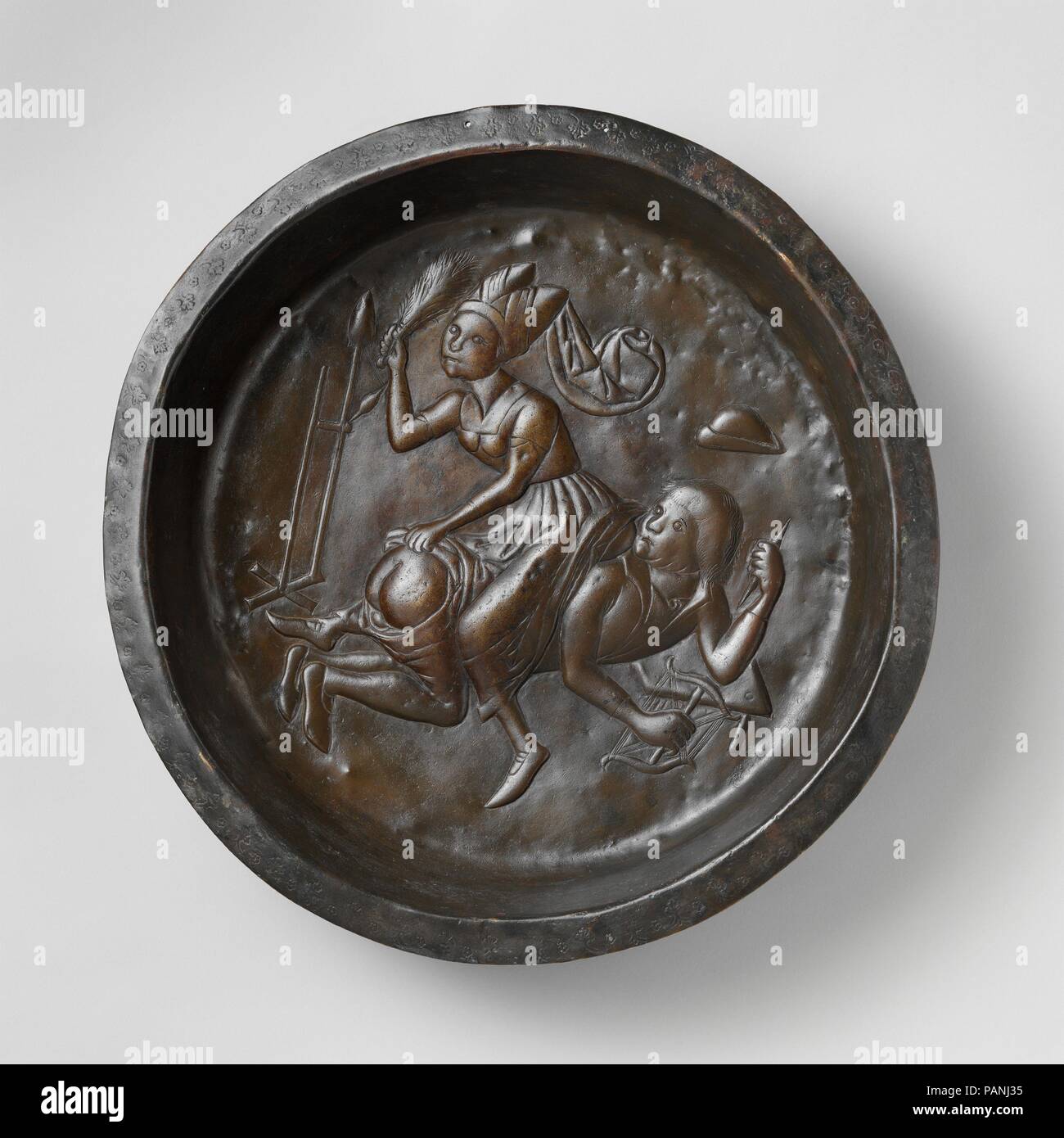 Plate with Wife Beating Husband. Culture: Netherlandish. Dimensions: Overall: 3 7/8 x 20 1/4 in. (9.8 x 51.5 cm). Date: ca. 1480.  The scene on this copper plate is usually thought to represent Aristotle being ridden by Phyllis, but it may be more accurately identified as a general depiction of a woman's tyrannical rule.   Spinning has throughout the ages been considered the work of women. By the time this plate was made, a relatively sophisticated type of spinning wheel had been developed, as seen in an illustration in Das Mittelalterliche Hausbuch of about 1480. The object to the left in thi Stock Photo