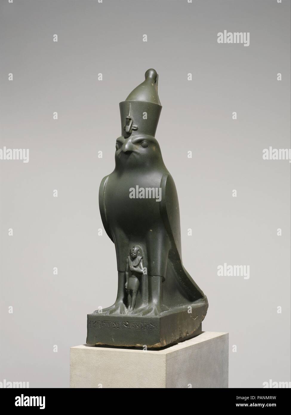God Horus Protecting King Nectanebo II. Dimensions: H. 72 cm (28 3/8 in.); W. 20 cm (7 7/8 in.); D. 46.5 cm (18 5/16 in.). Dynasty: Dynasty 30. Reign: reign of Nectanebo II. Date: 360-343 B.C..  The pharaoh Nectanebo II often invoked a very close connection-even a merging-between himself and the falcon god of kingship, Horus.  In fact, Nectanebo II was the focus of a cult in which he was referred to as 'Nectanebo-the-Falcon,' which could indeed be what is represented by this striking conjunction of a powerful falcon and the monarch. This idea seems to be supported by the fact that Horus is not Stock Photo