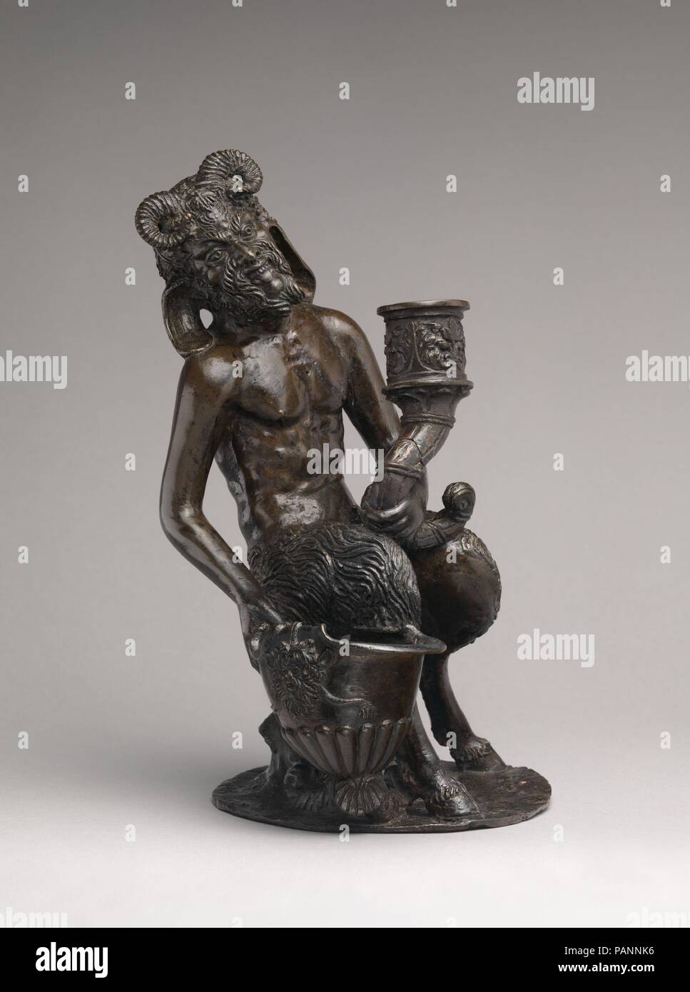 Seated Satyr, with an inkwell and a candlestick. Culture: Northern Italian. Dimensions: Overall (confirmed:) 10 × 6 1/4 × 6 1/2 in. (25.4 × 15.9 × 16.5 cm). Date: ca. 1530-40.  Bronzes in the Louvre and in the Wallace Collection, London, are virtually identical to this one, except that the horns are differently fashioned in each, and the Linsky bronze bears a special feature--a small rodent--brusquely chased into the tree trunk alongside a bit of sprouting foliage. The candlestick, in the form of a cornucopia, has been broken and mended.  It is difficult to say where bronzes of this model were Stock Photo