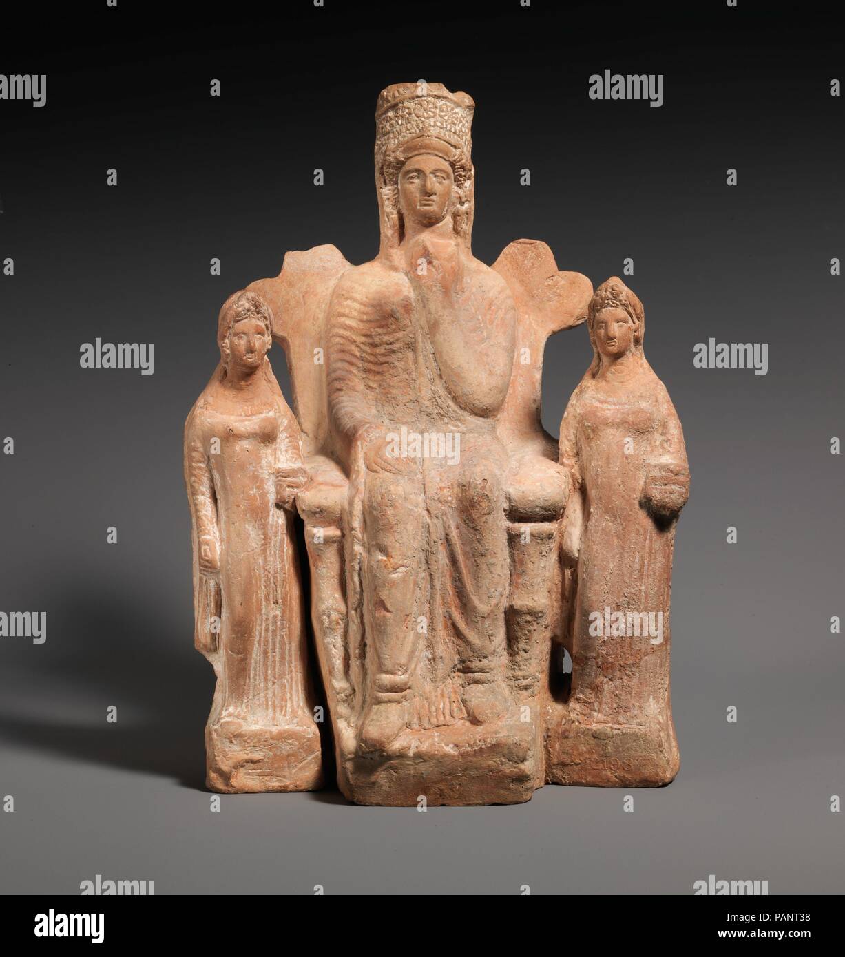 Terracotta statuette of an enthroned  goddess between two attendants. Culture: Cypriot. Dimensions: h. 10 13/16 in. (27.5 cm). Date: 4th century B.C..  This figurine is one of the most completely preserved of a group of enthroned goddesses from Kition. The seated goddess is flanked at either side by a standing attendant. The group is hollow and was mold-made in three parts; the two separately molded attendants are made to fit very closely against the sides of the goddess' throne. Both figures were joined to the throne at the back before firing. Museum: Metropolitan Museum of Art, New York, USA Stock Photo