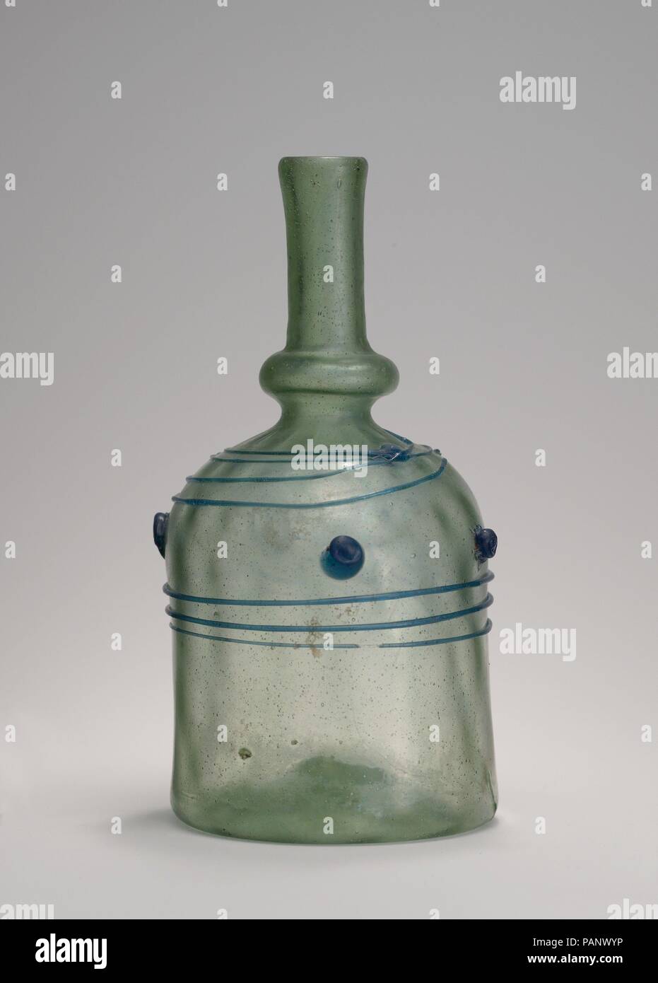 Bottle with Blue Trails. Dimensions: H. 6 11/16 in. (17 cm)  Max. Diam. 3 1/8 in. (7.9 cm). Date: 12th century.  This appealing pale green bottle was initially blown into a mold with narrow vertical ribs and then inflated so that the ribs appear in very shallow, nearly imperceptible relief. A long, thin trail of dark blue glass spirals around the object, forming an irregular pattern. Additional, shorter trails form a festooned design around the base of the neck, and four small blue blobs dot a larger band created by the spiraling trail. Bottles of this shape and decorated with blobs of glass i Stock Photo