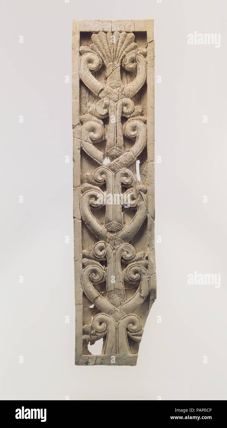 Furniture plaque carved in relief with volutes and a palmette. Culture: Assyrian. Dimensions: 9.84 x 2.32 x 0.39 in. (24.99 x 5.89 x 0.99 cm). Date: ca. 8th century B.C..  This ivory panel was found in a storage room in Fort Shalmaneser, a royal building at Nimrud that was used to store booty and tribute collected by the Assyrians while on military campaign. Like many other panels from the same storage room, it was part of a chair or couch back or the headboard of a bed. Twenty pieces of furniture were discovered stacked in orderly rows in this room, where they had been stored before the destr Stock Photo