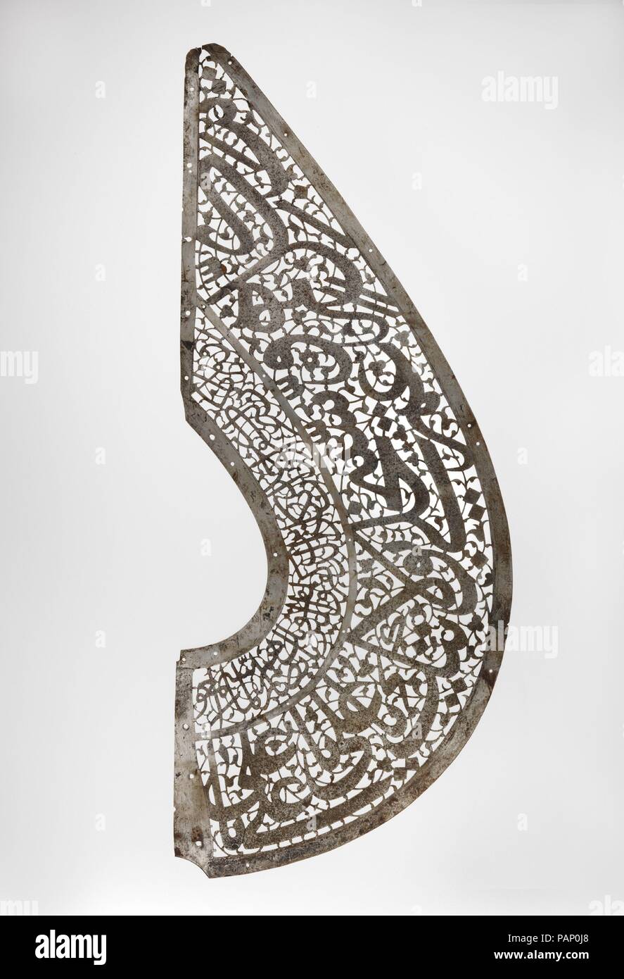Fragment of a Standard ('alam). Dimensions: Gr. H. 9 1/2 in. (24.2 cm)  Gr. L. 23 3/4 in. (60.3 cm). Date: 17th century.  This fragment is the right half of a pear-shaped steel standard which would have been originally framed by a twisted steel cord ending in a pair of outward-facing dragon heads. The form echoes one of the many types depicted in battle paintings from the sixteenth century royal manuscript of the Shahnama of Shah Tahmasp. Standards from this period have pierced scrolling vegetal designs and talismanic inscriptions. Here, the inscriptions are Shi'i in tone and include the Nad-i Stock Photo