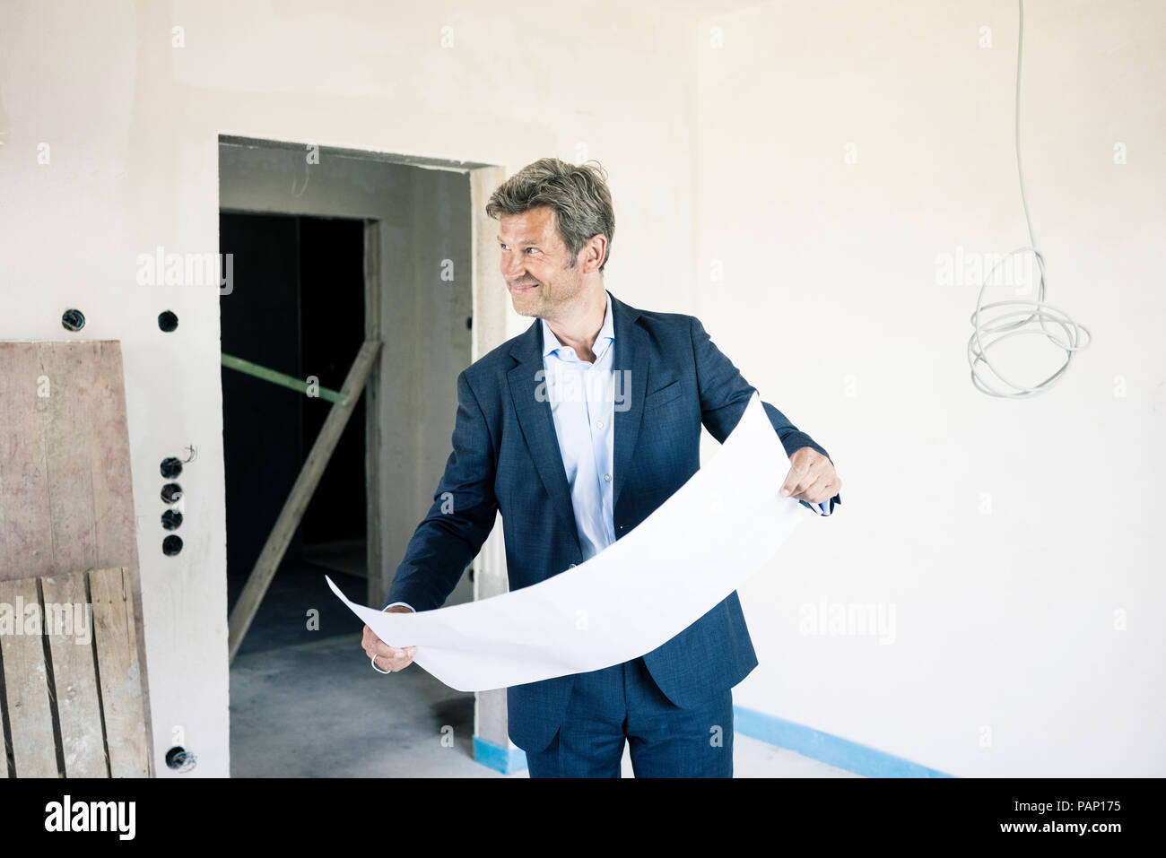 Smiling architect with blueprint in building under construction Stock Photo